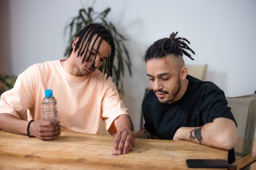 Free Two friends having a casual conversation at a wooden table indoors. Stock Photo