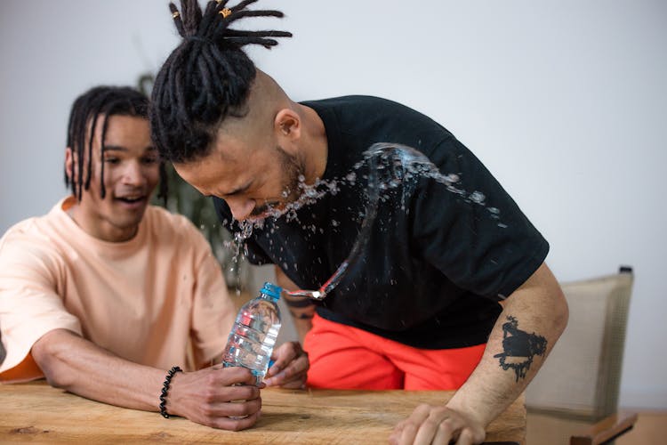 Man Squeezing The Bottle Of Water On His Friend