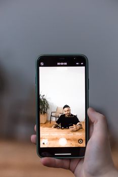 Close-up of a hand holding a smartphone filming a person indoors.