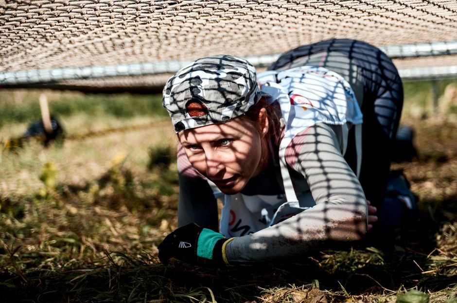 A young woman crawls under a net in an outdoor training or obstacle course.
