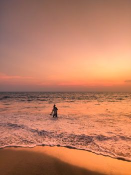 A serene beach scene at sunset with a silhouette standing in the gentle waves.