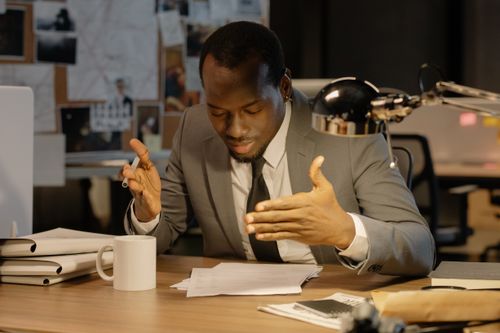 Free African American man in a gray suit reviewing papers at an office desk. Stock Photo