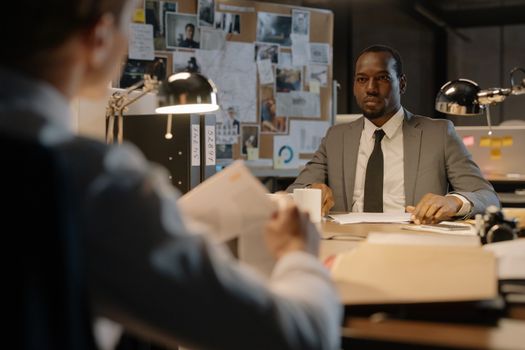 Business discussion in a well-lit office with a focus on paperwork and detective work.
