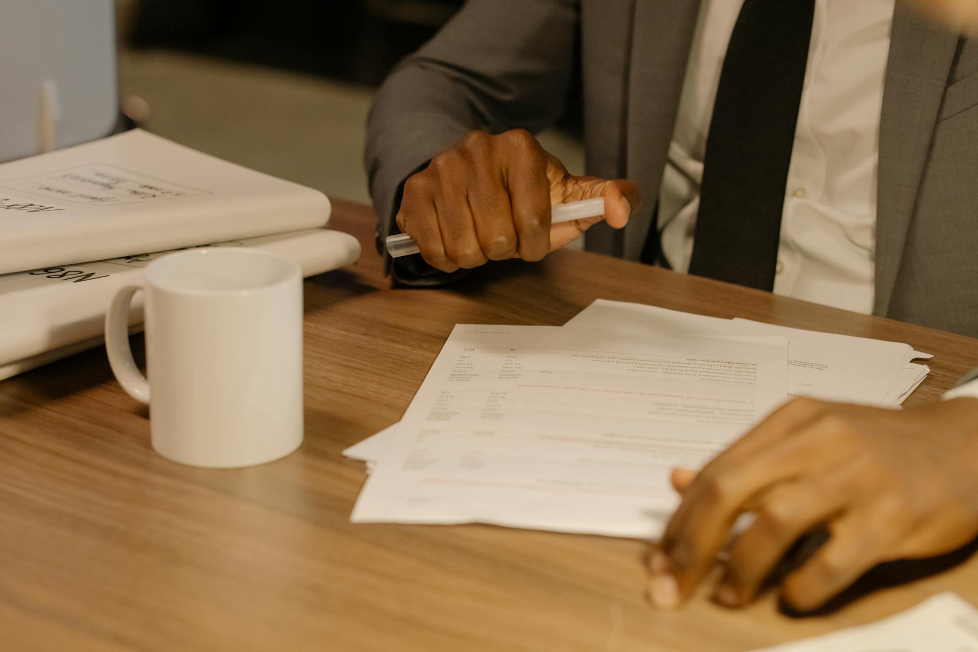 Close-up of a businessman holding and reviewing documents on a wooden desk.