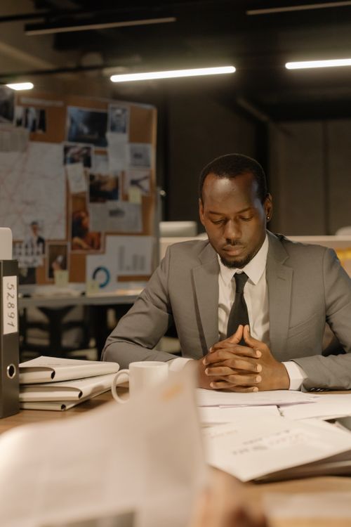 Free Businessman in a suit deeply focused on reviewing papers in a modern office setting. Stock Photo