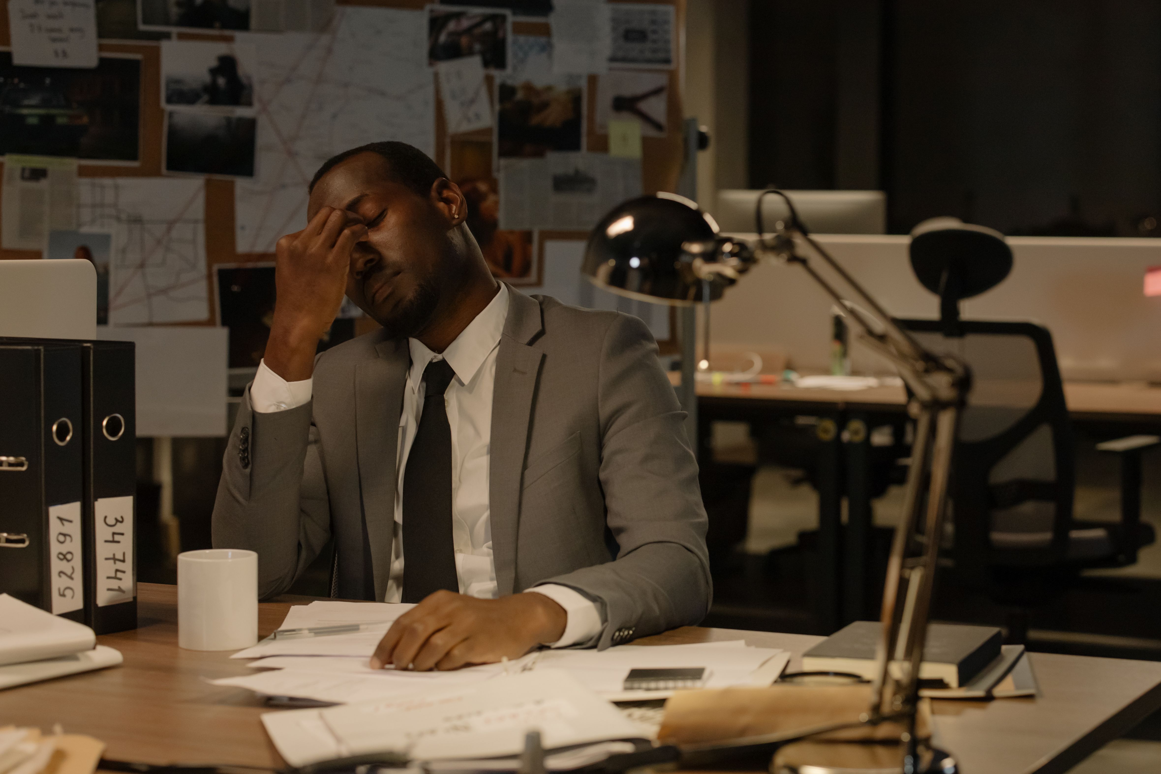 tired student sitting at desk with piles of papers, clock showing late night, parent looking concerned