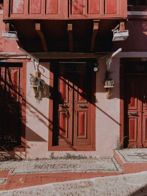 Sunlit rustic house facade featuring a vintage wooden red door and intricate details.