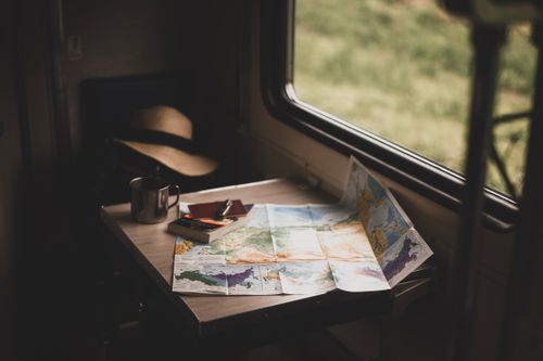 Una mappa del mondo, una tazza e un cappello su un tavolo, pianificazione di un viaggio in treno in Europa.