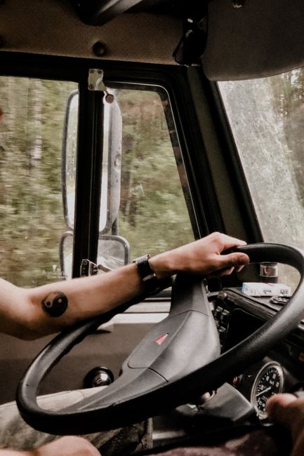 Man with yin-yang tattoo driving through forested area, view from inside vehicle.