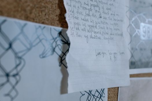 A close-up image of a handwritten letter pinned to a cork board in soft focus.
