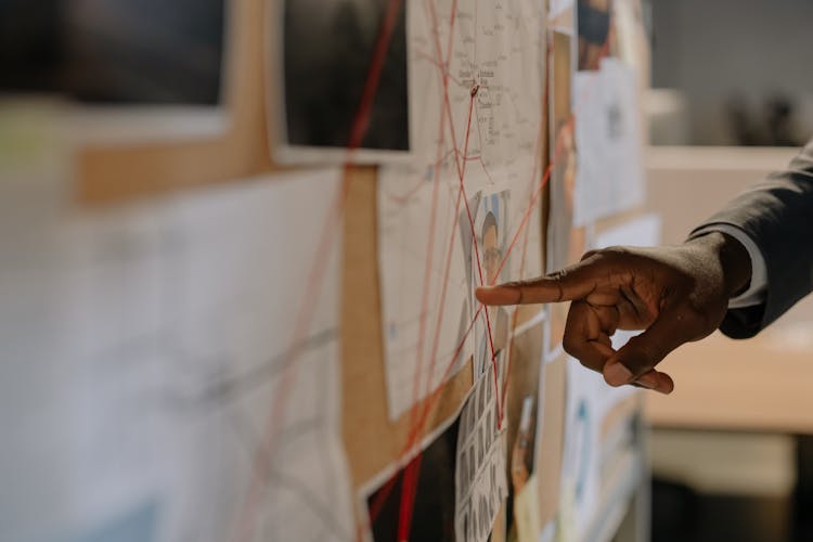 Close-Up Shot Of A Person Pointing At Evidence Board