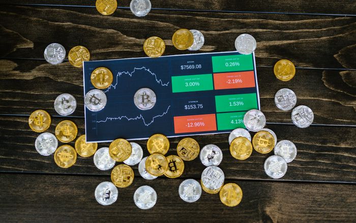 Bitcoin coins scattered around a stock chart on a dark wooden table, symbolizing cryptocurrency investment.