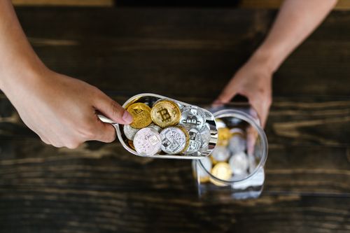 Free Close-up of hands scooping assorted cryptocurrency coins into a jar on a wooden surface. Stock Photo