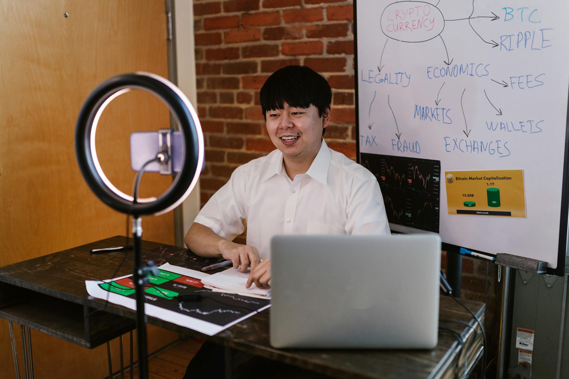 Man discussing cryptocurrency economics with ring light and laptop, engaging content creation.