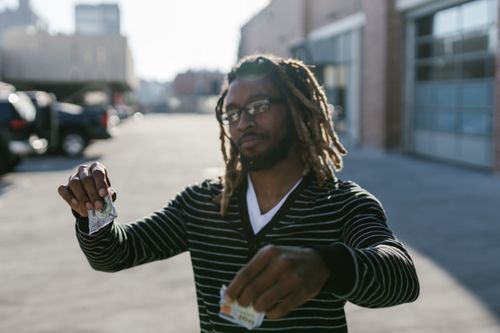 Free A young man with glasses and dreadlocks tearing a banknote in an urban outdoor setting. Stock Photo