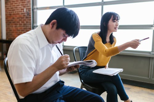 Man and Woman Sitting on Chairs while Taking Down Notes