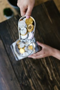 Hands pouring visually textured cryptocurrency coins into a transparent container.