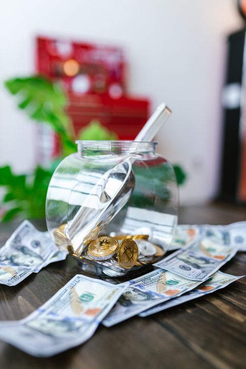 Free A clear jar filled with bitcoin coins surrounded by dollar bills, representing digital currency investment. Stock Photo