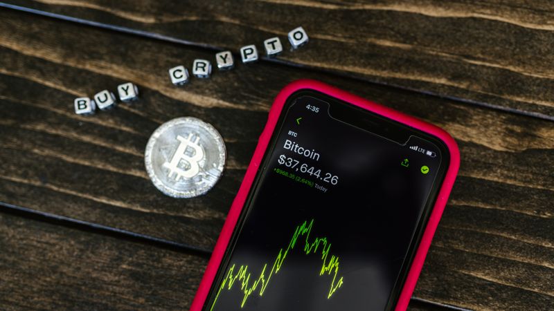 Smartphone showing bitcoin price with a physical coin and text representing cryptocurrency investment.