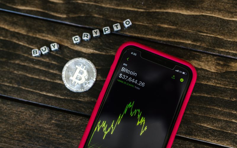 Close-up of a smartphone showing bitcoin price next to a physical coin, representing the kind of crypto portfolio I manage inside Trust Wallet