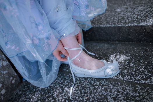 Close-up of a delicate lace shoe being tied on a stone step, showcasing intricate design.
