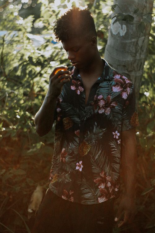 Free Black man in floral shirt surrounded by trees, sunlight highlighting a serene moment. Stock Photo