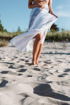 A woman in a flowing dress stands barefoot on a sunny beach with her legs partially visible.