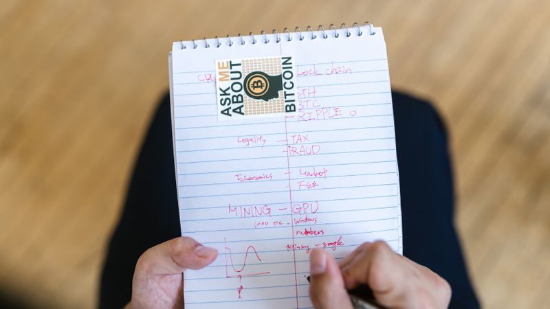 Close-up of a person writing notes about bitcoin and cryptocurrency on a notepad.