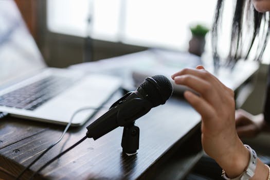 Close-up of a microphone and hand near a laptop, ideal for podcasting themes.