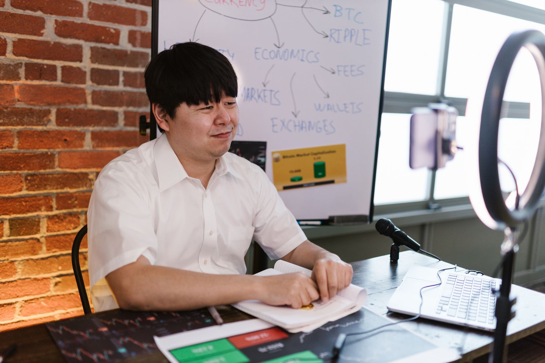 Man engaged in cryptocurrency blogging, using a ring light, microphone, and laptop, with a focus on Bitcoin and trading.