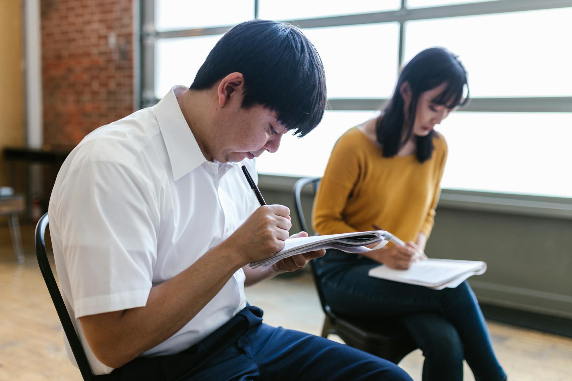 Two students intensely taking notes during a lecture inside a modern classroom.