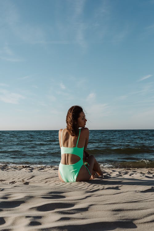 Woman in Green Bikini Sitting on Beach Shore