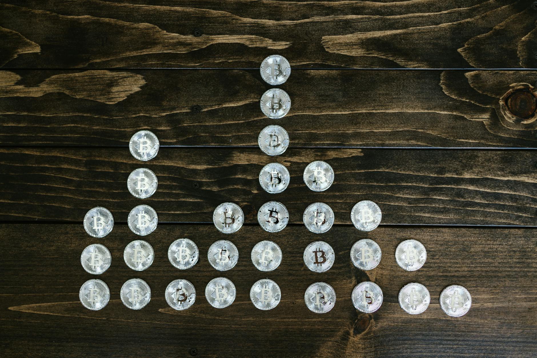 Silver bitcoin coins organized on a dark wooden table forming a visual pattern symbolizing cryptocurrency growth.