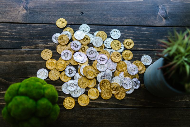 Gold and silver bitcoin coins mixed on a wooden surface with potted plants.