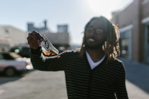 Free A man holds a burning cryptocurrency-themed bank note outdoors, symbolizing financial instability. Stock Photo