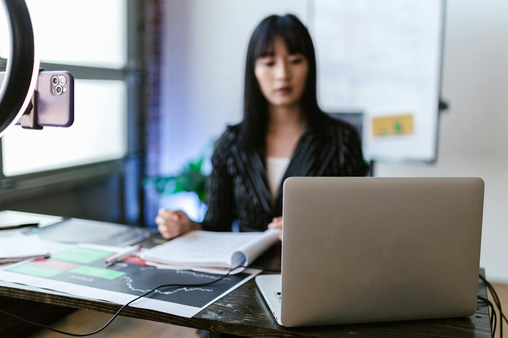 Focused woman trading stocks on a laptop in a modern office setting, capturing the essence of investment and technology.