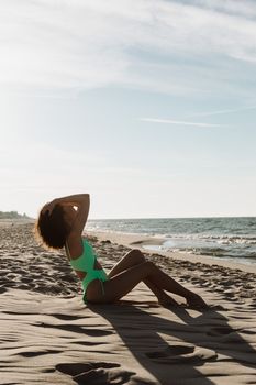 Woman in green swimsuit posing on a sandy beach by the ocean on a sunny day.