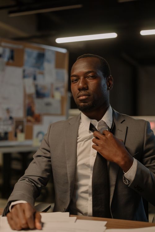 Free A poised businessman in a suit sits at a desk in an office, exuding confidence. Stock Photo