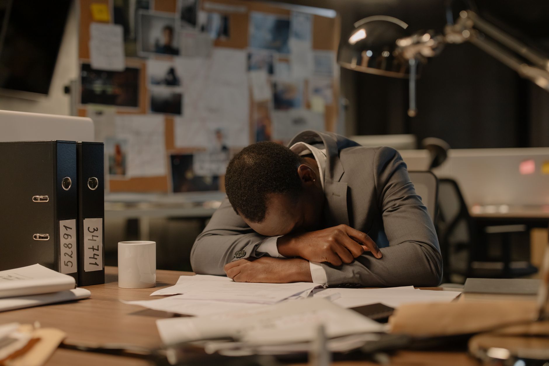 A tired businessman in a suit asleep at his office desk surrounded by documents and papers.