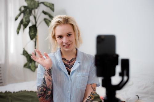 Free Tattooed woman with blonde hair smiling and recording video using a smartphone indoors. Stock Photo