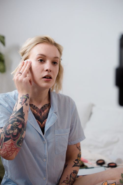 Free A tattooed woman with blonde hair applies makeup in a casual indoor setting. Stock Photo