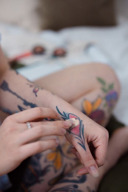 Free Close-up of a tattooed hand applying foundation cream, showcasing body art and skincare routine. Stock Photo