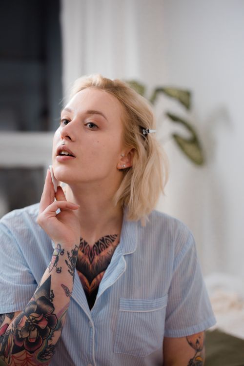 Free A young woman with tattoos applies skincare cream indoors, showcasing beauty and self-care. Stock Photo