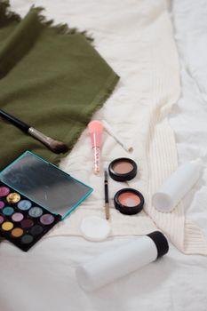 A collection of makeup products including eyeshadow palette and blush on white fabric.