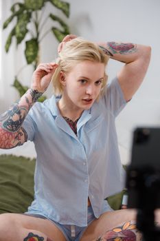 Tattooed woman styles hair with clip in cozy indoor setting.