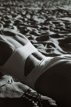 A grayscale image of a woman in a swimsuit lying on sandy beach, emphasizing texture and contrast.