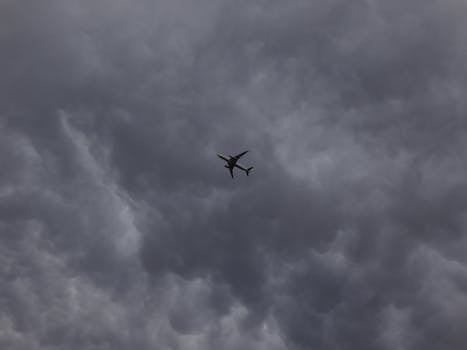 A silhouette of an airplane flying amidst dark storm clouds, showcasing aviation and weather phenomena.