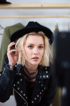 Fashionable woman in a black hat and leather jacket posing indoors.