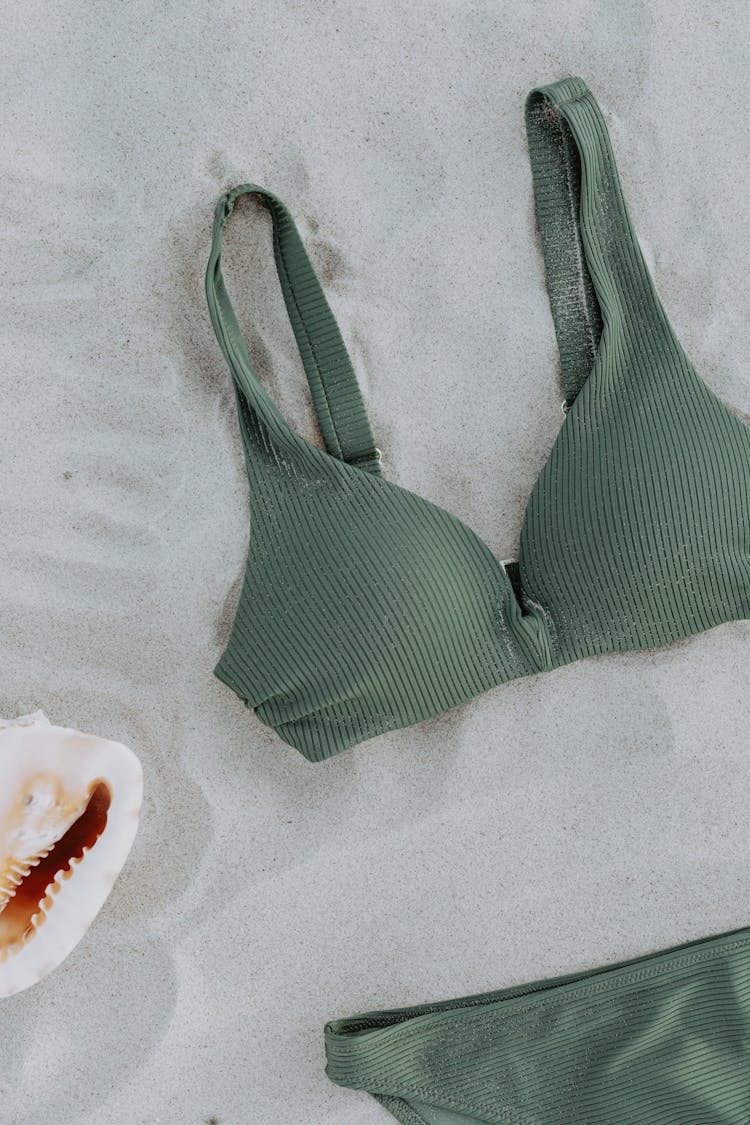 Green Bikini Costume And Big Seashell Lying On Sand