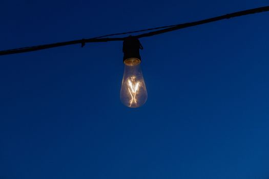 An illuminated light bulb hanging on a wire against a deep blue twilight sky, creating a serene ambiance.